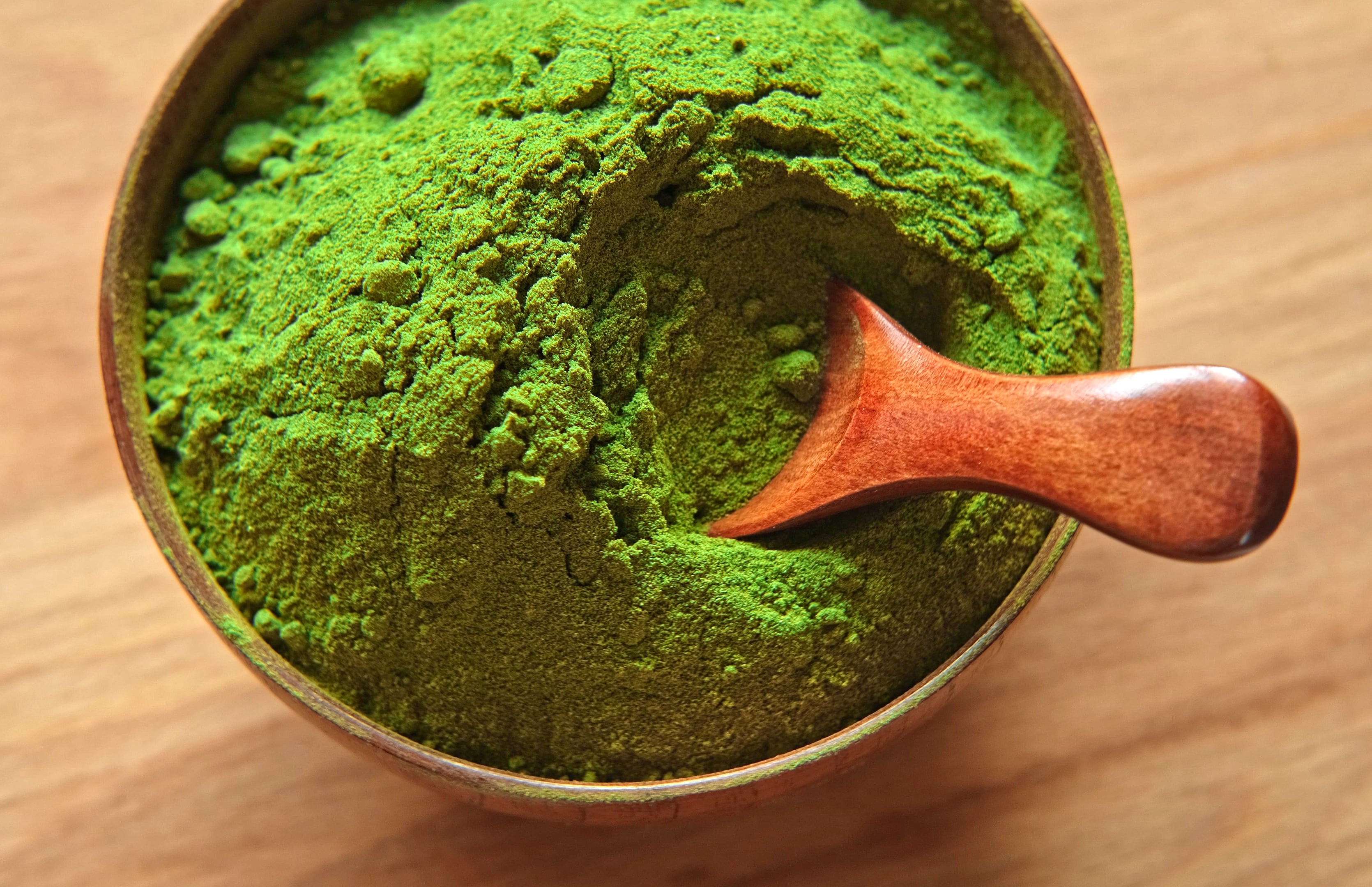 Wooden spoon with powdered matcha tea in a bowl spinning on natural background. Matcha powder. Top view, Closeup. Finely ground green powder. Japanese culture. Healthy eating with high antioxidants. Superfood rotation. biosupplement for drink shake preparation. Health. Grounded spinach powder and whole wheat flour. Matcha tea powder, spinach, chlorella, moringa, wheatgrass, or broccoli powder.